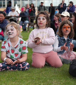 Three children sitting on the grass with their faces painted.